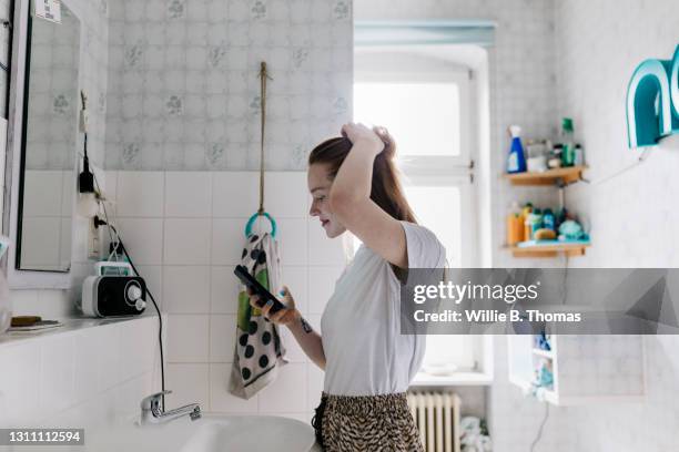 girl looking at smartphone while getting ready in bathroom - vestir se fotografías e imágenes de stock