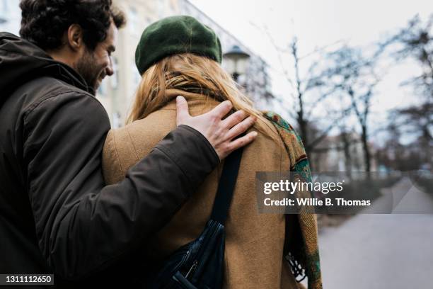 man with his arm around girlfriend while out walking together - arm umlegen stock-fotos und bilder