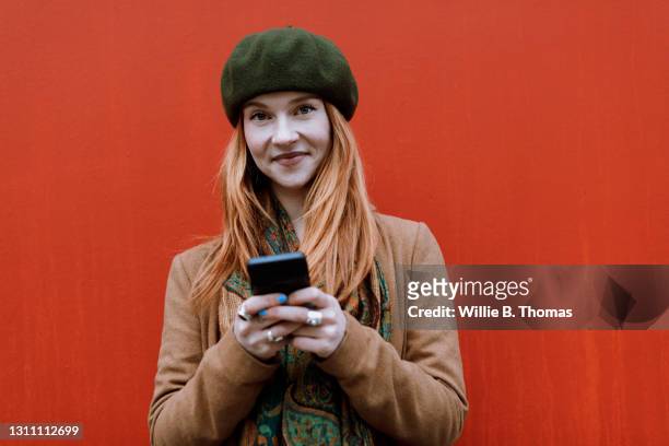 portrait of woman with red hair using smartphone - beige hat stock pictures, royalty-free photos & images