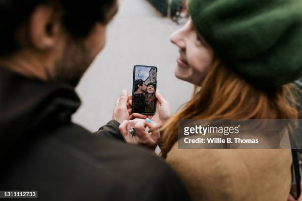 couple smiling while looking at selfies on smartphone together - showing smartphone stock pictures, royalty-free photos & images