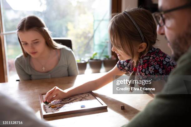 father, teenager and younger child playing a board game together at a dining table - snakes and ladders stock pictures, royalty-free photos & images