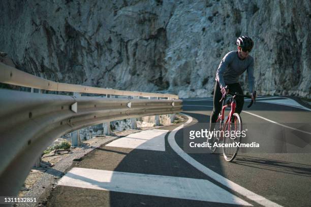 young man road bikes down coastal road in the morning - crash barrier stock pictures, royalty-free photos & images