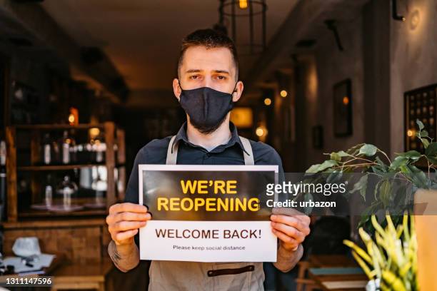 waiter holding "we're reopening" sing and wearing mask - reopening banner stock pictures, royalty-free photos & images