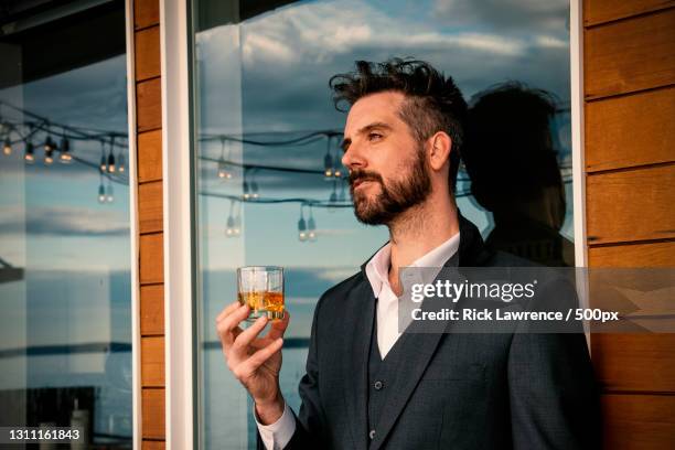 man drinking whisky on ice in glass while watching sunset,seattle,washington,united states,usa - whiskey stock-fotos und bilder