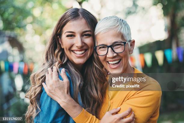 mother and adult daughter embracing during a garden party - mothers day stock pictures, royalty-free photos & images