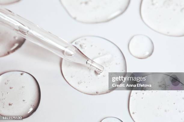 drop of gel or serum with air bubbles flow out from a pipette near other drops on a pastel white background. flat lay style and extreme close-up - säure stock-fotos und bilder