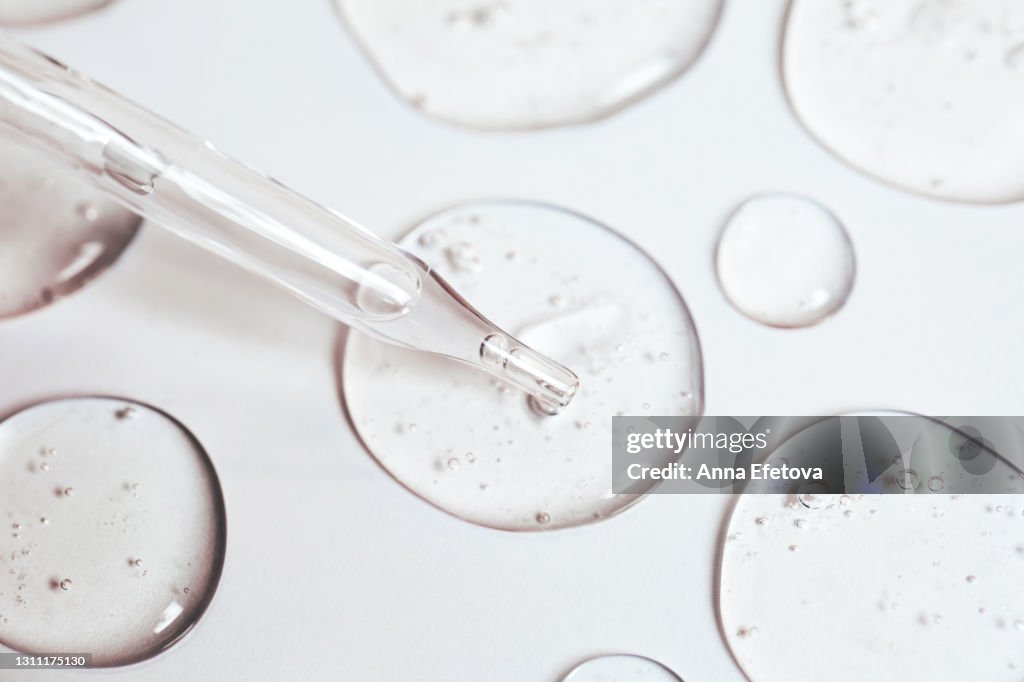 Drop of gel or serum with air bubbles flow out from a pipette near other drops on a pastel white background. Flat lay style and extreme close-up