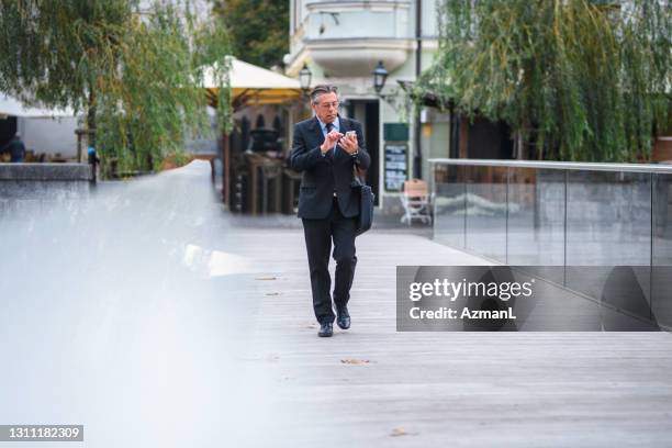 senior executive using smart phone during commute to work - man walking towards camera stock pictures, royalty-free photos & images