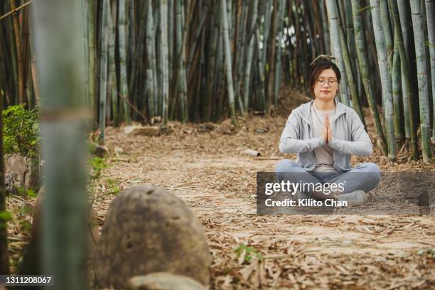 asian woman practicing tai chi in a bamboo forest - women practice yoga in the bamboo forest stockfoto's en -beelden