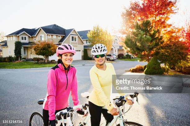 medium shot portrait of smiling mother and teenage daughter standing with bikes before road ride on fall afternoon - teenager cycling helmet stock pictures, royalty-free photos & images