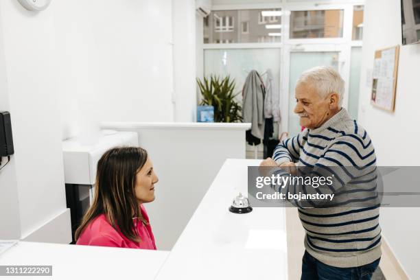 senior male patient at a doctors reception desk - medical administrator stock pictures, royalty-free photos & images