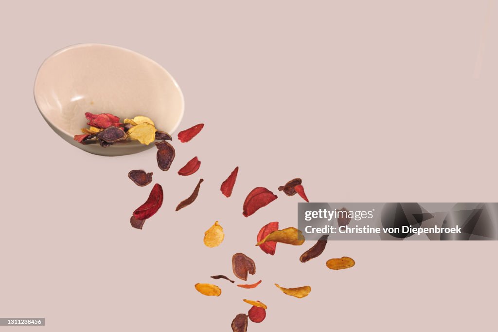 Flying fried chips and bowl on plain background