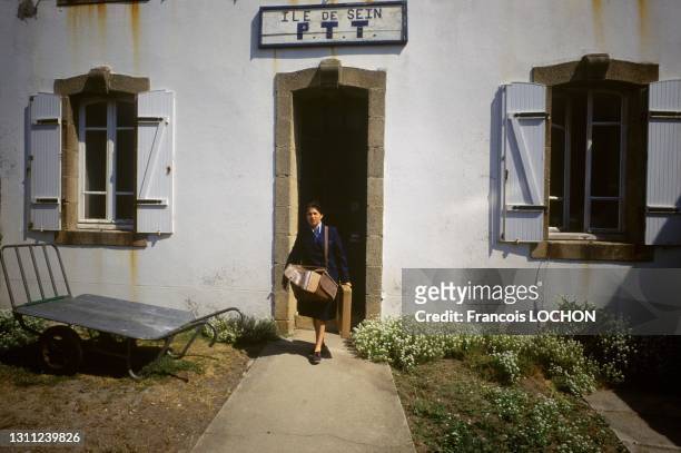 Femme fatrice sortant de la poste et portant un sac et un paquet sur l'Ile de Sein en juin 1988, Finistère.