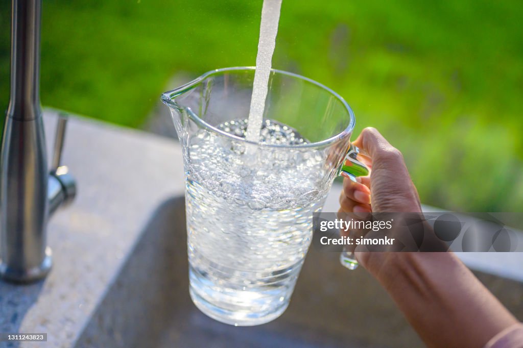 Woman's hand filling pitcher with water