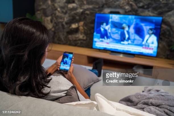 jeune femme observant des nouvelles à la télévision et au téléphone intelligent - événement d'actualité photos et images de collection