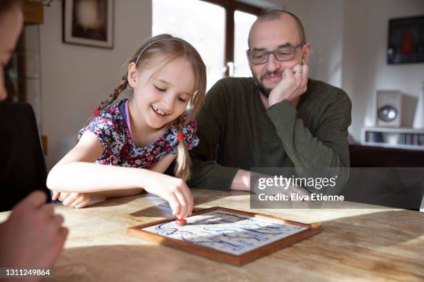 happy girl (8-9) playing a board game with father and teenage sister at a dining table - snakes and ladders stock pictures, royalty-free photos & images