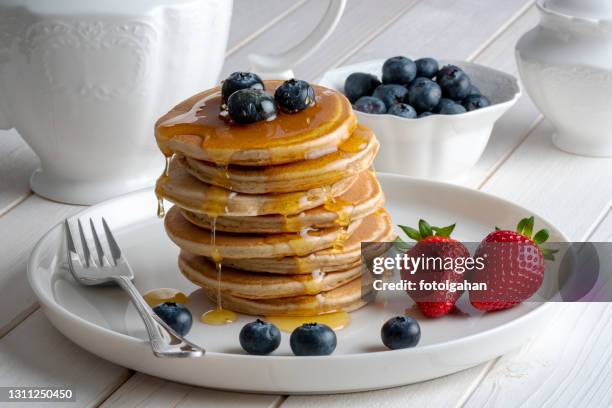 close-up delicious pancakes, with fresh blueberries, strawberries and maple syrup on a light background. sweet honey flows from a stack of pancake stock photo - raspberry syrup stock pictures, royalty-free photos & images