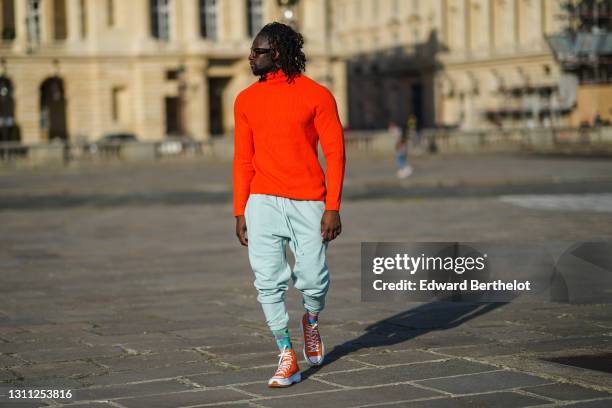 Cali Chiki wears glasses from Emmanuelle Khanh, a bold red / orange wool turtleneck pullover from Bershka, sportswear jogger pale green pants from...