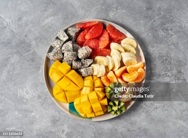 plate of tropical fruits (grapefruit, banana, orange, kiwi, mango, and dragon fruit) on gray background - fruitschaal stockfoto's en -beelden