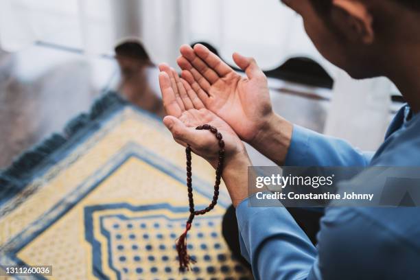 muslim man with open palm praying at home during month of ramadan - islamismo fotografías e imágenes de stock