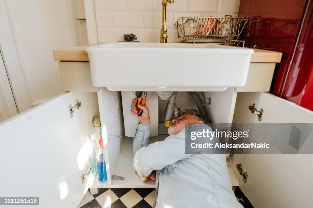 uomo maturo che risolve problemi idraulici in cucina - under sink foto e immagini stock