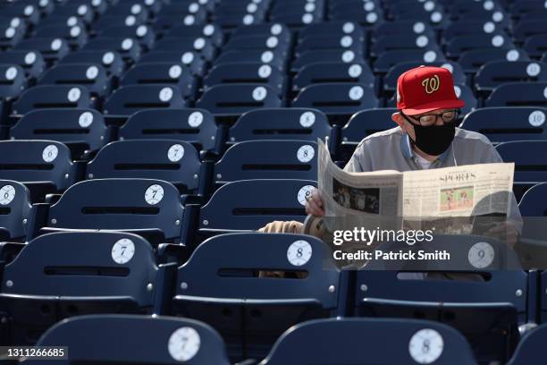 Fan wears a protective face covering due to the coronavirus and reads the sports section of the Washington Post before the Washington Nationals 2021...