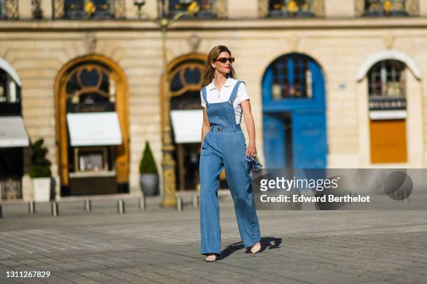 Natalia Verza @mascarada.paris wears a blue denim overall jumpsuit, a white polo shirt, a Louboutin mini bag, pointed high heels shoes from...