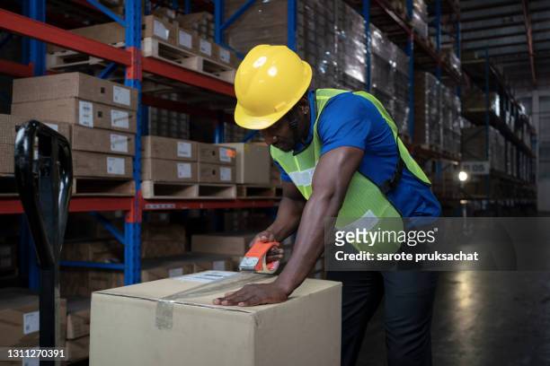 warehouse worker sealing cardboard boxes for shipping in a large warehouse - opening a box stockfoto's en -beelden