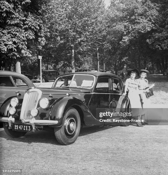 Femmes posant avec une voiture ancienne lors du concours d'élégance automobile de Paris, dans le bois de Boulogne, le 23 juin 1949.