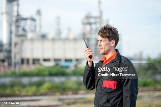 petroleum engineers discussing plan by walkies talkie to control room while standing near oil refinery visible in the background. oil and gas industry business. - cbs stock pictures, royalty-free photos & images