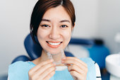 Asian young attractive woman holding orthodontic retainers in dental clinic. Invisalign orthodontics concept.