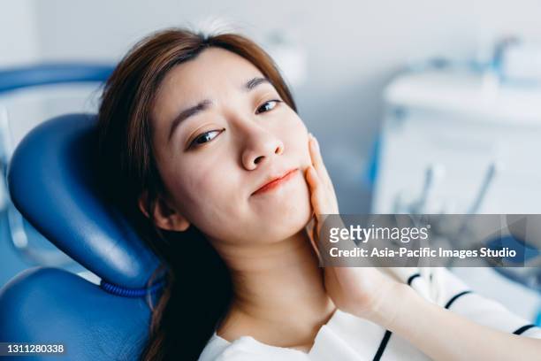 jeune femme asiatique se sentant la douleur, retenant sa joue avec la main au bureau du dentiste. concept de mal de dents. - maxillaire humain photos et images de collection