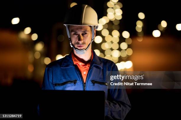 petroleum engineers working on laptop near oil refinery visible in the background. oil and gas industry. - hydrocarbon stock pictures, royalty-free photos & images