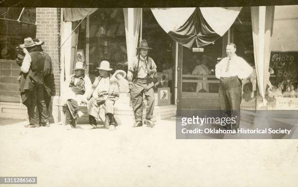 Portrait of a group of unidentified men, including members of the Osage Nation, as they pose in front of a shop, Hominy, Oklahoma, circa 1918. The...