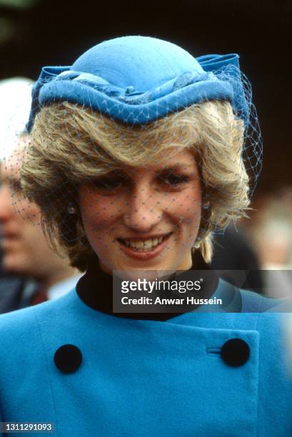 Diana, Princess of Wales, wearing a blue coat with black buttons and a matching hat with netting and a bow on the back, smiles during a walkabout in...