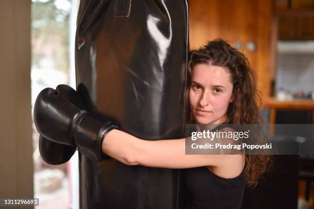 portrait of young female boxer woman hugging punching bag indoors - muay thai stock pictures, royalty-free photos & images