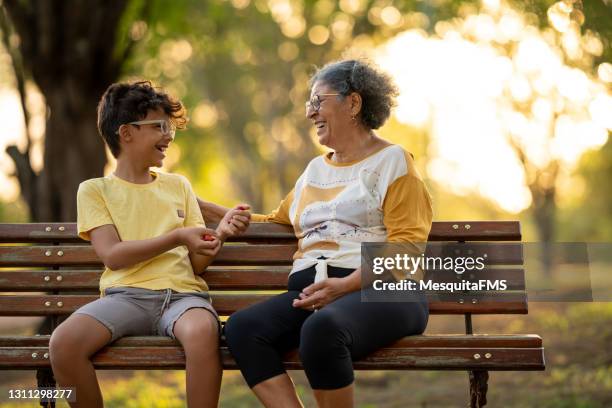 großmutter und enkel sitzen auf der bank auf dem platz - conversation sunset stock-fotos und bilder