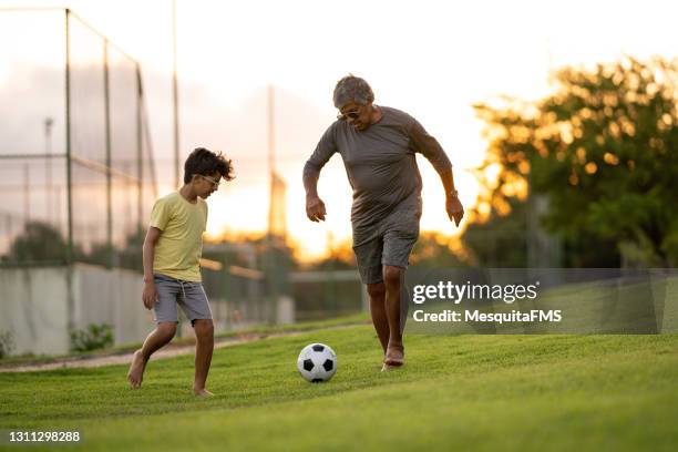 boy playing football on the grass with grandfather - senior kicking stock pictures, royalty-free photos & images