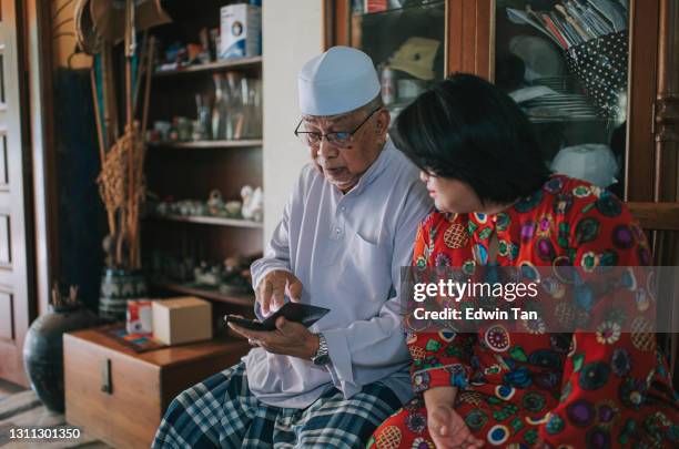 malaysischer großvater schaut auf smartphone sitzen neben seiner enkelin mit down-syndrom während hari raya familientreffen - malay culture stock-fotos und bilder