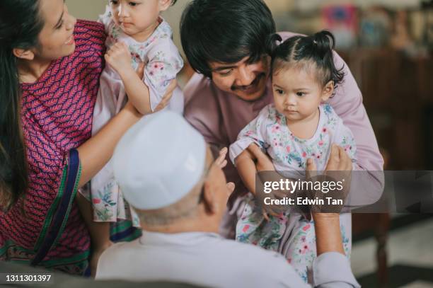 malay muslim grandson and his family in traditional costume showing apologize gesture to his grandfather during aidilfitri celebration malay family at home celebrating hari raya - malay couple stock pictures, royalty-free photos & images