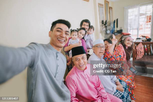malaysian malay family taking selfie photo looking at camera waving at home celebrating hari raya - malay songkok stock pictures, royalty-free photos & images