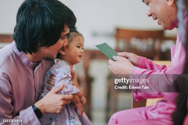 hari raya malay muslim baby girl en traje tradicional recibe un paquete de dinero en hari raya aidilfitri / eid-ul-fitr celebración en la sala de estar - bolsita fotografías e imágenes de stock