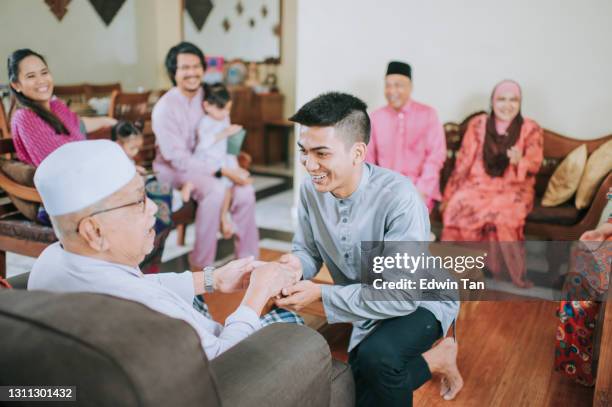 malénieto musulmán con ropa tradicional mostrando gesto de disculpa a su abuelo haji durante la celebración aidilfitri familia malay en casa celebrando hari raya - 80s living room fotografías e imágenes de stock