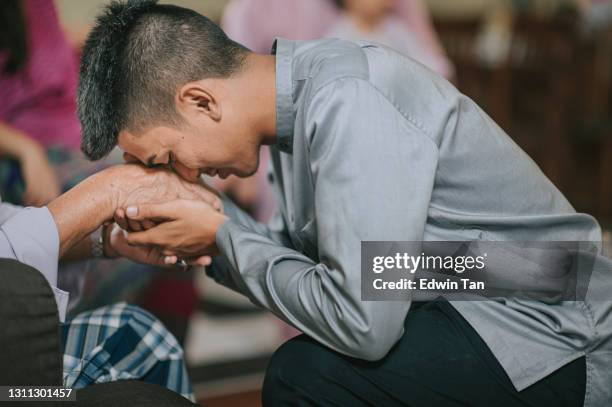 malay muslimischen enkel in traditioneller tracht zeigt entschuldigung geste an seinen großvater während aidilfitri feier malay familie zu hause feiern hari raya - hari raya celebration stock-fotos und bilder