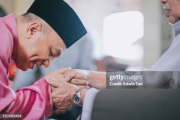 malay muslimischen sohn in traditioneller tracht zeigt entschuldigung geste an seinen vater während aidilfitri feier malay familie zu hause feiern hari raya - hajj stock-fotos und bilder