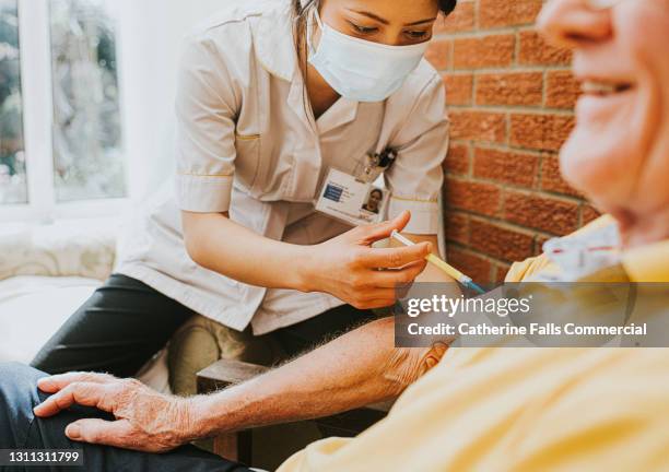 female nurse gives an elderly man an injection in his arm - covid vaccination stock pictures, royalty-free photos & images