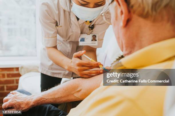 female nurse gives an elderly man an injection in his arm - vaccine uk stock pictures, royalty-free photos & images