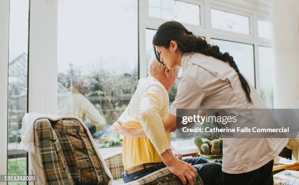 young care assistant helps an elderly gent put on his jumper - asistencia de la comunidad fotografías e imágenes de stock