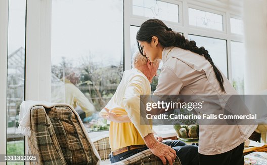 Young care assistant helps an elderly gent put on his jumper Young care assistant helps an elderly gent put on his jumper