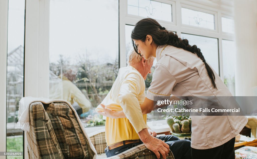 Young care assistant helps an elderly gent put on his jumper